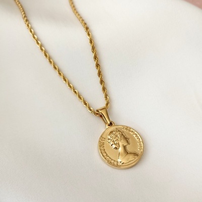 Colar dourado com pendente redondo em relevo sobre tecido branco