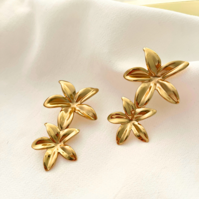 Brincos dourados em forma de flores com cinco pétalas sobre tecido branco