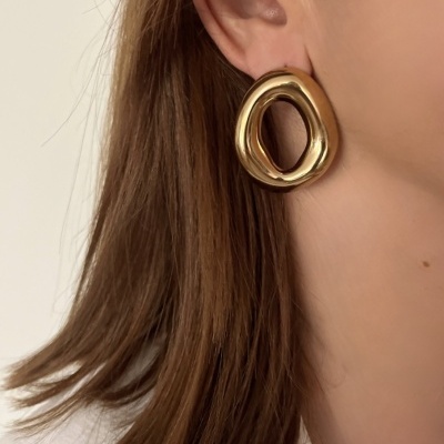 Brincos dourados arredondados irregulares em orelha feminina