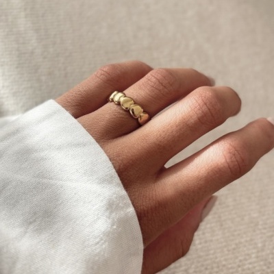 anel dourado com corações no dedo médio de mão feminina com camisa branca