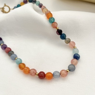 Colar de contas coloridas com esferas douradas sobre tecido branco