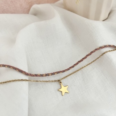 Colar dourado com estrela e cordão trançado sobre tecido branco