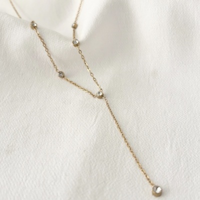 Colar dourado com pedras transparentes sobre tecido branco
