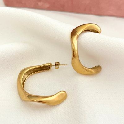 Brincos dourados de argola aberta sobre tecido branco