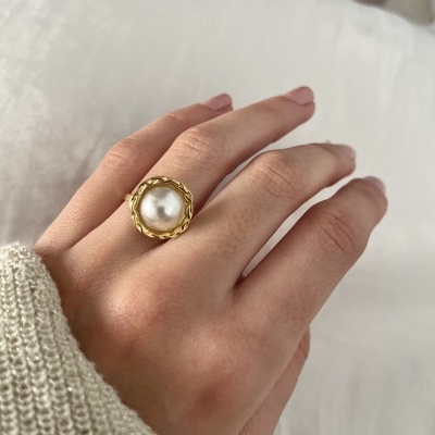 Anel dourado com pérola branca numa mão com suéter bege