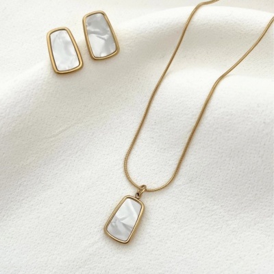 Conjunto de joalharia dourada com detalhes brancos sobre tecido branco