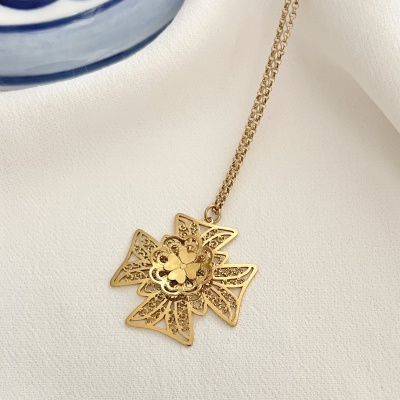 Colar dourado com pendente em forma de cruz decorada sobre tecido branco