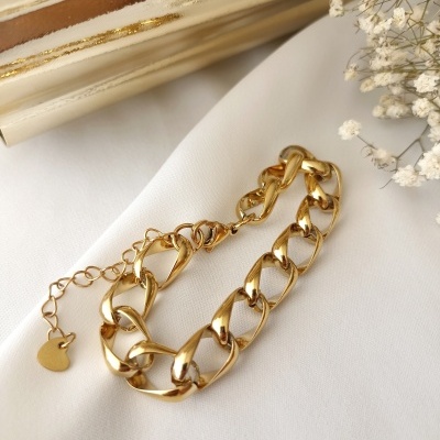 Pulseira dourada com elos grandes e pendente coração sobre tecido branco