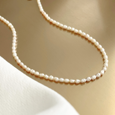 Colar de pérolas brancas com fecho dourado sobre superfície dourada