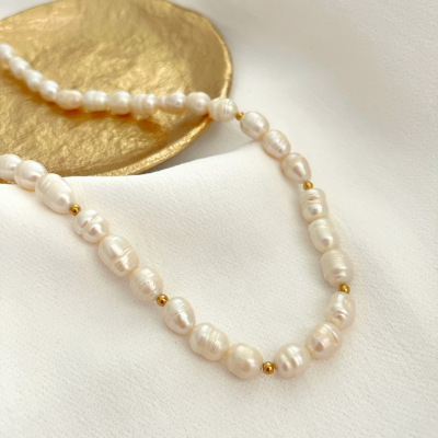 Colar de pérolas brancas com contas douradas sobre tecido branco e prato dourado