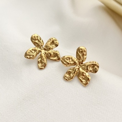 Brincos dourados em forma de flor com textura martelada sobre tecido branco