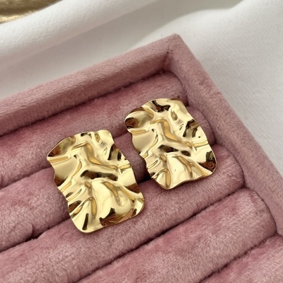 Par de brincos dourados ondulados numa caixa de veludo rosa