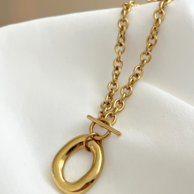 Colar dourado com pendente oval sobre tecido branco