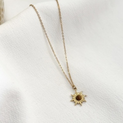 Colar dourado com pendente em forma de sol com pedra castanha sobre tecido branco