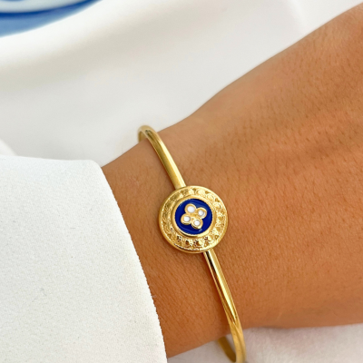 Pulseira dourada rígida com medalha decorada azul e dourada no pulso