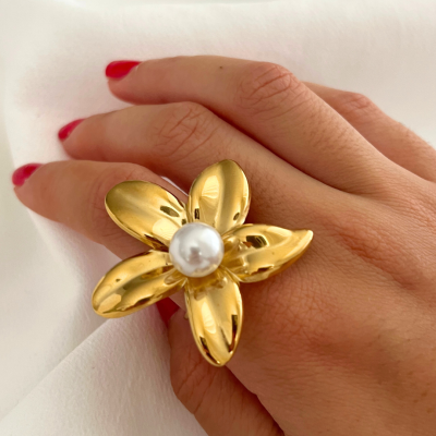 Anel dourado em forma de flor com pérola branca no centro numa mão com unha vermelha.