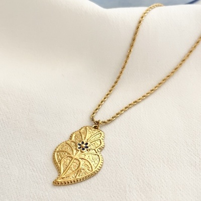 Colar dourado com pendente em forma de folha sobre tecido branco