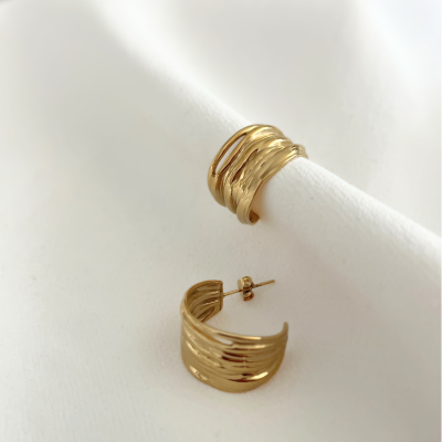 Brincos e anel dourados com textura ondulada sobre tecido branco