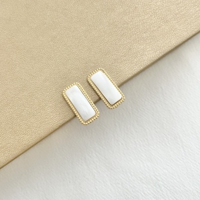 Brincos retangulares dourados com preenchimento branco sobre superfície bege e fundo branco