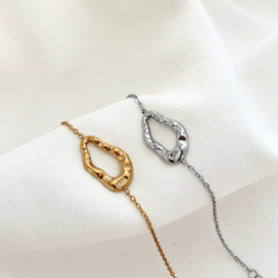 Duas pulseiras metálicas, uma dourada e outra prateada, sobre tecido branco