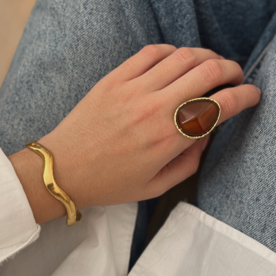 Mão com anel e bracelete dourados sobre calças de ganga azuis