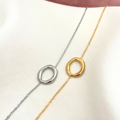Pulseiras delicadas prateada e dourada com pendentes ovais sobre tecido branco