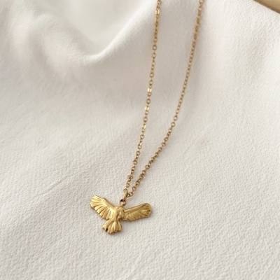 Colar dourado com pendente de ave sobre tecido branco