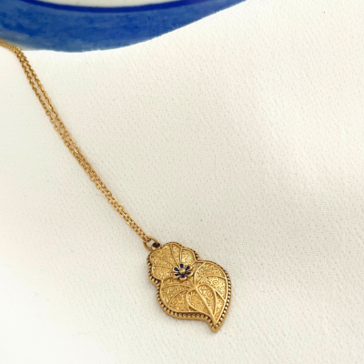 Colar dourado com pendente em forma de folha e detalhe azul