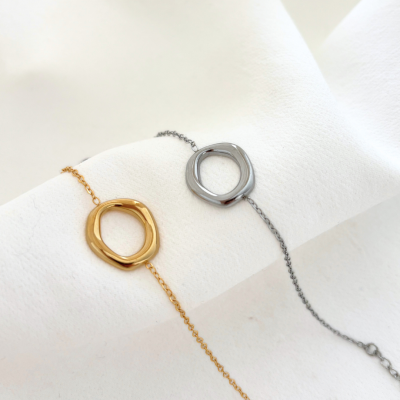 Pulseiras dourada e prateada com pingente oval irregular em tecido branco.