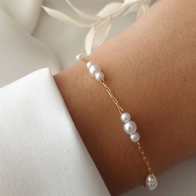 Pulseira dourada com pérolas brancas no pulso