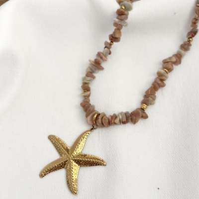 Colar com pendente de estrela do mar dourada em corrente de pedras irregulares cor de rosa sobre tecido branco