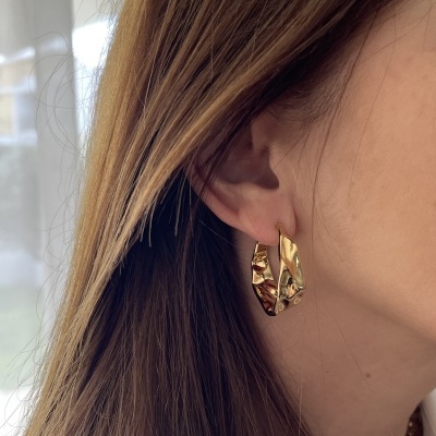 Brinco de argola dourado texturizado na orelha de uma mulher