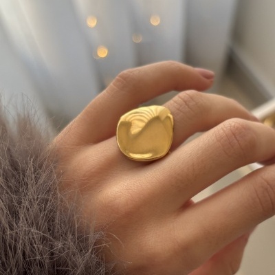 Anel dourado liso usado na mão com tecido felpudo cinza