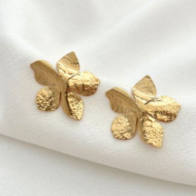 Brincos dourados em forma de flor com textura martelada sobre tecido branco