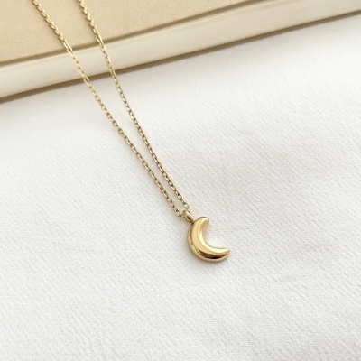 Colar dourado com pendente de lua crescente sobre tecido branco