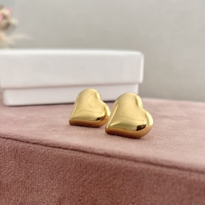 Brincos dourados em forma de coração sobre superfície rosa aveludada