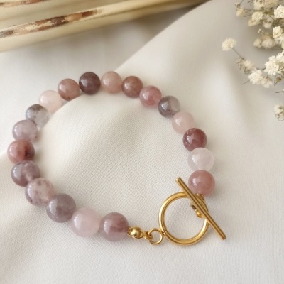 Pulseira de contas de pedra rosa e roxa com fecho dourado sobre tecido branco
