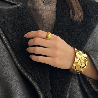 Mão feminina com anel e pulseira dourada, casaco preto e blusão castanho