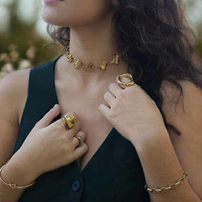 Mulher com colar choker dourado, anéis e pulseiras douradas, veste vestido preto