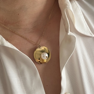 Colar dourado com medalhão redondo e pérola falsa numa pessoa com camisa branca