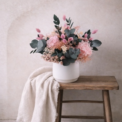 Arranjo floral em vaso branco sobre banco de madeira com tecido branco
