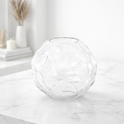 Vaso redondo de vidro transparente com textura ondulada sobre superfície branca de mármore.