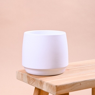 Vaso branco de cerâmica simples sobre mesa de madeira clara