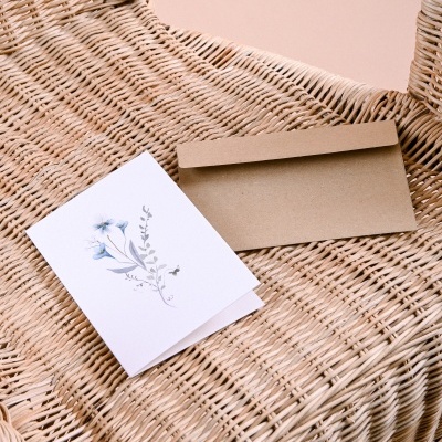 Cartão branco com flores e envelope castanho sobre cadeira de verga