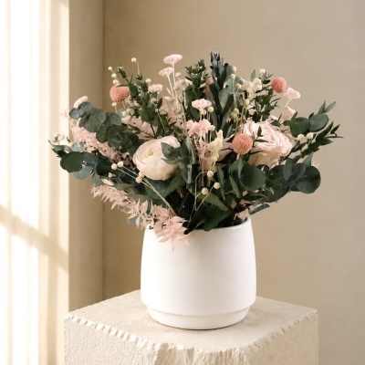 Arranjo floral com flores rosas e verdes num vaso branco sobre pedestal bege