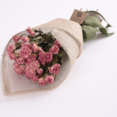 Ramo de rosas secas cor-de-rosa embaladas em papel e rede com laço verde e etiqueta