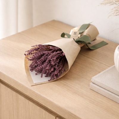 Ramo de flores secas roxas em papel castanho com laço verde sobre mesa de madeira clara