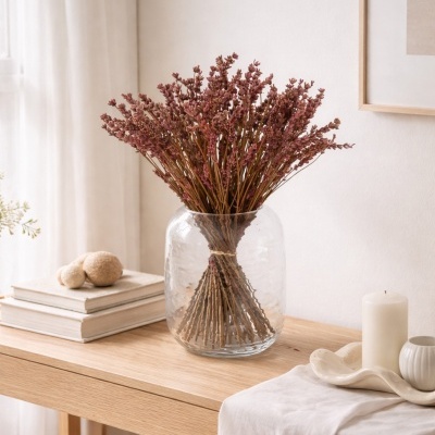 Vaso de vidro com flores secas rosa sobre mesa de madeira com objetos decorativos e livros
