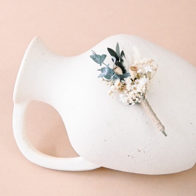 Ânfora cerâmica branca com flores secas amarradas em fundo bege