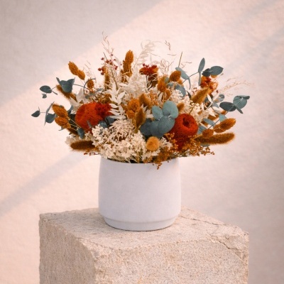 Arranjo floral seco em vaso branco fosco sobre bloco de pedra bege